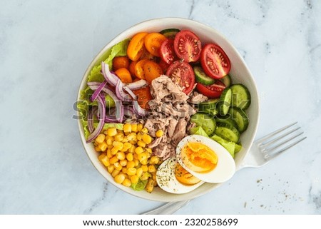 Tuna salad with egg, vegetables and corn in a white bowl, white background, top view.