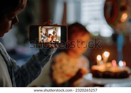Two beautiful kids, little preschool boys celebrating birthday and blowing candles on homemade baked cake, indoor. Brother making picture with smartphone. Selective focus