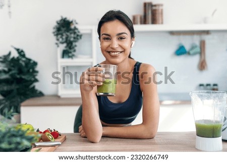 Shot of athletic smiling woman drinking smothie while listening music with earphones in the kitchen at home. Royalty-Free Stock Photo #2320266749
