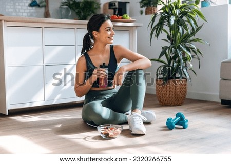 Shot of athletic woman drinking healthy protein shake while sitting on floor in the kitchen at home Royalty-Free Stock Photo #2320266755