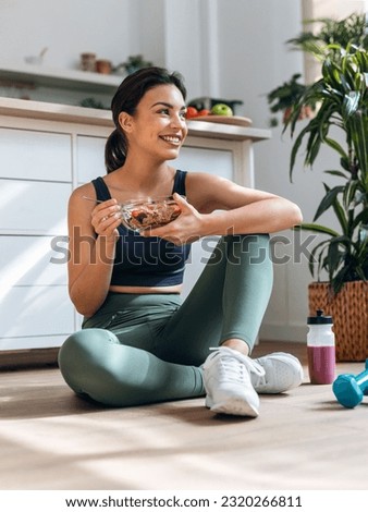Shot of athletic woman eating a healthy bowl of muesli with fruit sitting on floor in the kitchen at home Royalty-Free Stock Photo #2320266811