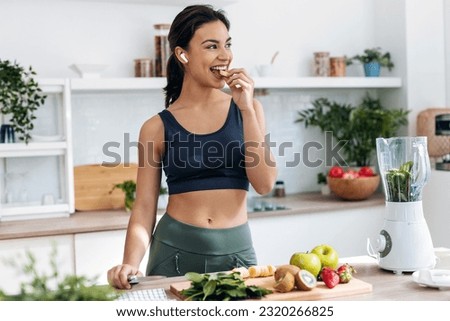 Shoot of athletic woman cutting fruits and vegetables to prepare a smoothie while listening to music with earphones in the kitchen at home Royalty-Free Stock Photo #2320266825