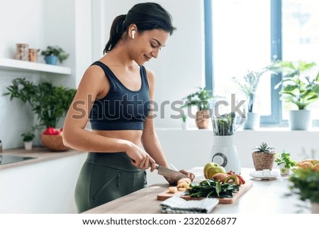 Shoot of athletic woman cutting fruits and vegetables to prepare a smoothie while listening to music with earphones in the kitchen at home Royalty-Free Stock Photo #2320266877