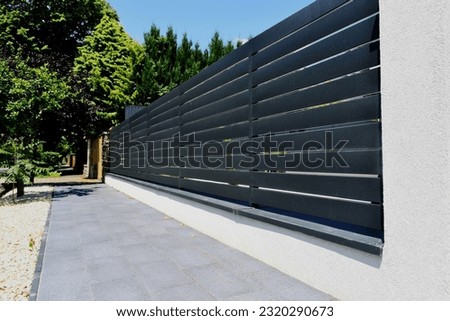 gray aluminum fence and gate. horizontal panels. narrow gaps.  powder coated finish. diminishing perspective view. modern fence design concept. concrete sidewalk. white stucco base and fence piers Royalty-Free Stock Photo #2320290673
