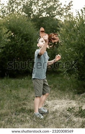 a little boy in aviator glasses plays with a wooden airplane in the park in summer