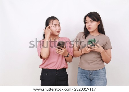 Two confused asian women holding cell phone Isolated on white background Royalty-Free Stock Photo #2320319117