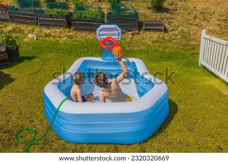Close up view of two boys in inflatable outdoor swimming pool playing water basketball on backyard on sunny summer day. Sweden.