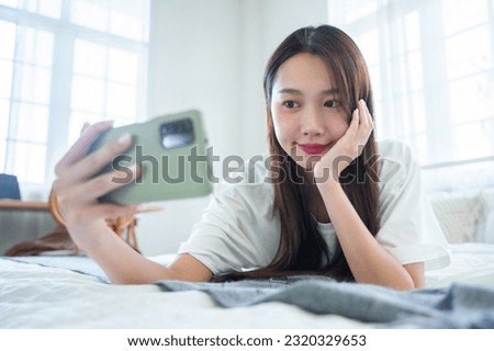 Portrait of Happy Beautiful Asian Korean girl taking selfie photos with smartphone or mobile phone on bed at home.