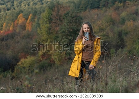 Happy girl takes pictures on smartphone of beautiful autumn forest. Young woman uses mobile phone while walking in nature.