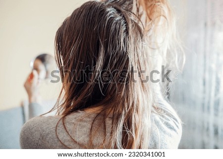 Woman checking dirty oily and greasy hair looking in mirror at home. Bad hair care cosmetics concept. Back view Royalty-Free Stock Photo #2320341001