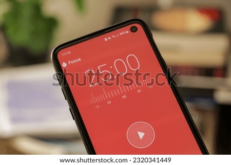 A phone with a red 25-minute timer to study with the pomodoro method on a blurry background. Perfect for students planning their time studying, doing homework, being productive. Royalty-Free Stock Photo #2320341449