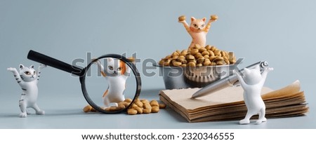 Cute toy kittens next to bowl, dry cat food, notebook, magnifier and pen. Сoncept of choosing the best pet food. Сoncept of studying the nutritional properties of animal feed. Toy world. Close-up