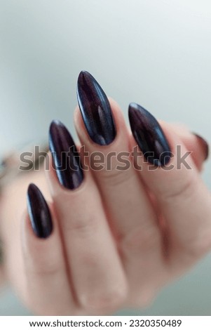 Female hands with long nails and black purple manicure holding a bottle of nail polish