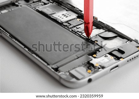 Smartphone tweaking and hacking during manufacturing crisis - red screwdriver inside dismantled cell phone symbolises the invisible hand of Chinese engineers inside telecommunication devices worldwide Royalty-Free Stock Photo #2320359959