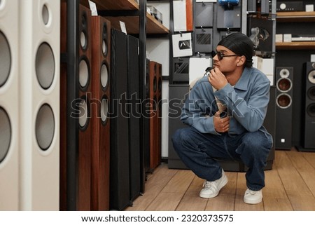 Full length portrait of young black man choosing professional speakers in music store, copy space Royalty-Free Stock Photo #2320373575