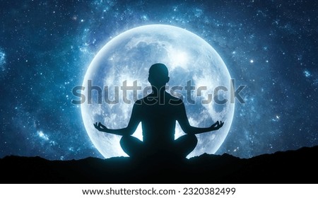 Woman silhouette sitting in yoga lotus pose against full blue Moon in the sky. Night sky landscape. Psychology and esoteric Royalty-Free Stock Photo #2320382499