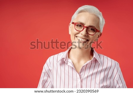 Portrait of happy senior woman wearing stylish red eyeglasses isolated on red background, vision concept. Attractive smiling gray haired businesswoman, confident manager looking at camera 