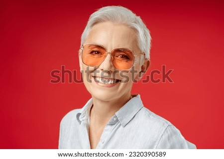 Portrait of smiling gray haired senior woman wearing stylish sunglasses isolated on red background. Attractive businesswoman, CEO, manager looking at camera. Successful business 