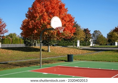 An outdoor basketball court seen in the fall season with a beautiful trees in the background with colorful leaves