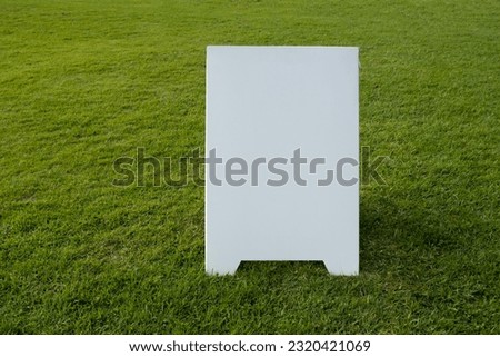 Background texture of a blank white advertising information board place outdoor on green and healthy grass lawn. Mockup template of a wedding welcome sign in garden. Empty copy space for your design.