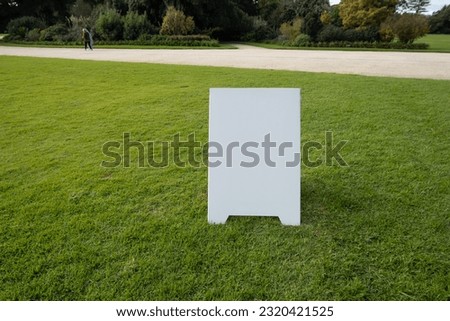 Background texture of a blank white advertising information board place outdoor on green and healthy grass lawn. Mockup template of a wedding welcome sign in a formal garden with footpath. copy space