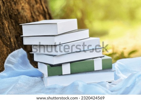 Stacking books on blue clothe beside the big tree trunk with morning sunlight. Early morning reading is benefit becasue you are well rested, and your brain is in peak condition for learning.