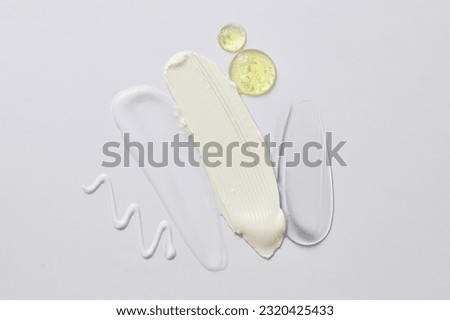 Natural skin care concept of serum drops in yellow color and some cosmetic texture smears. Cosmetic smudge on light background closeup