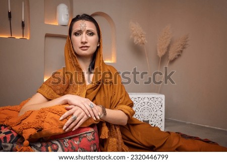 a beautiful young woman in an Indian dress is sitting on pillows, looking at the camera and smiling, selective focus, close-up