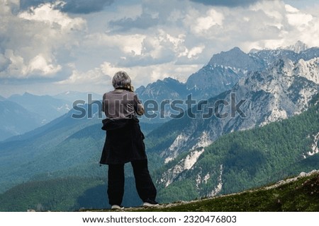 Older woman  taking photos of mountains covered with fog and snow; cloudy sky in background