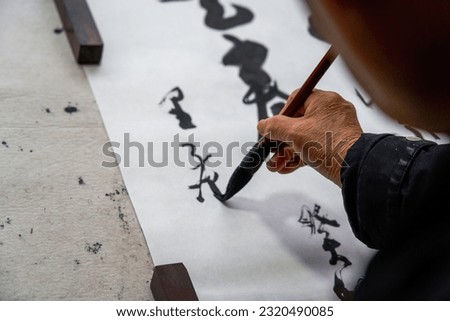 An old Chinese calligrapher is writing brush characters, creating Chinese calligraphy works.
Translation: Spring comes, the god of wind arrives.