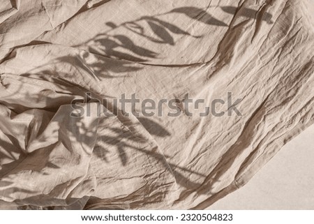 Crumpled linen fabric texture with folds in a sun light and lifestyle floral sunlight shadow. Aesthetic minimal bohemian neutral beige background