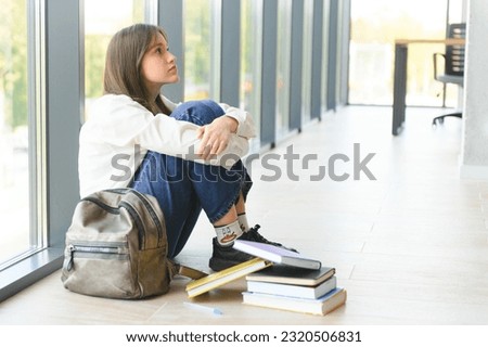 Upset teen girl sit on floor sadly look out window worried about teenage problem at school and communication with parent. Worried girl tensely suffer about bullying at school, unrequited love with boy Royalty-Free Stock Photo #2320506831