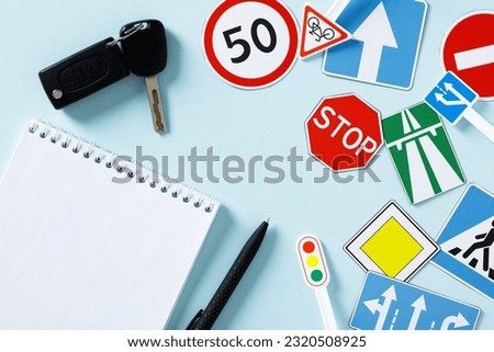 Flat lay paper notebook, car keys, road sign on blue background. Driving school concept. 