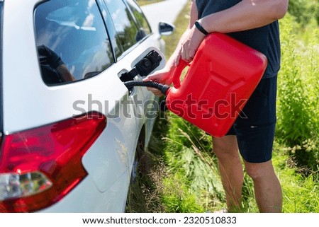 Force majeure, problems on the road. Selective focus, noise. Adventures on the road, problems with fuel. The driver fills up the empty tank of the car from a red canister on the side of the road Royalty-Free Stock Photo #2320510833