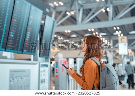 Happy asian woman traveller checking flight schedule departures board in airport terminal hall in front of check in counters. Tourist journey trip concept Royalty-Free Stock Photo #2320527825