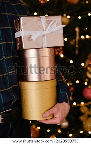 A man holds three gift boxes in front of a Christmas tree. Golden crusts for the holidays