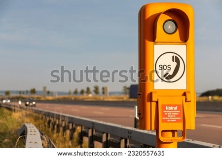 Highway Safety: Orange SOS Calling Box on German Highway, Translation: SOS, emergency call, please lift the flap and press the button! Wait until the emergency call from the car insurer. Royalty-Free Stock Photo #2320557635