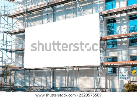 Blank white advertisement hanging on the scaffolding of modern building under construction.Reconstruction of a building with white billboard.
