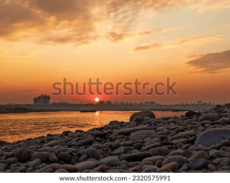 A beautiful sunset at River Indus with beautiful tumbled stones in the foreground. The mighty river Indus stays in the background with beautiful golden sky with scattered clouds. Distant small island