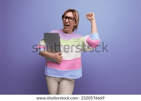 successful blond woman student with a laptop in her hands rejoices with happiness on a purple background