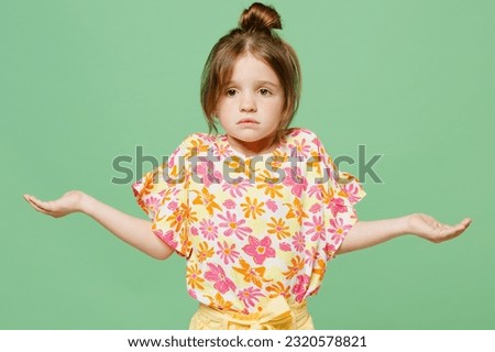 Little sad child kid girl 6-7 years old wears casual clothes shrugging shoulders speading hands isolated on plain pastel green background studio portrait. Mother's Day love family lifestyle concept Royalty-Free Stock Photo #2320578821