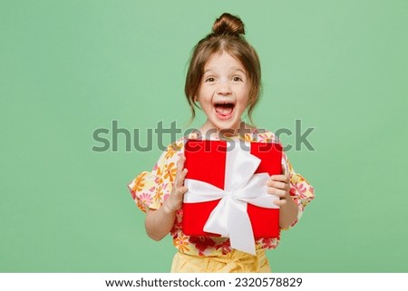 Little cute child kid girl 6-7 years old wear casual clothes have fun hold present box with gift ribbon bow isolated on plain pastel green background studio. Mother's Day love family lifestyle concept