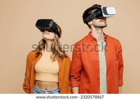 Young smiling caucasian happy couple two friends family man woman wear casual clothes together watching in vr headset pc gadget isolated on pastel plain light beige color background studio portrait