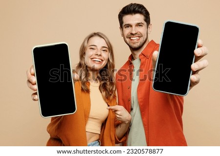 Young smiling couple two friend family man woman wear casual clothes hold in hand use showing close up mobile cell phone with blank screen workspace area together isolated on plain beige background Royalty-Free Stock Photo #2320578877