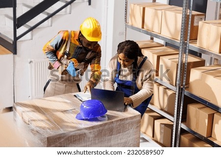 Order pickers team looking at customers list on laptop and clipboard, working in retail storehouse. Ecommerce warehouse african american employees fulfilling customer online purchase Royalty-Free Stock Photo #2320589507