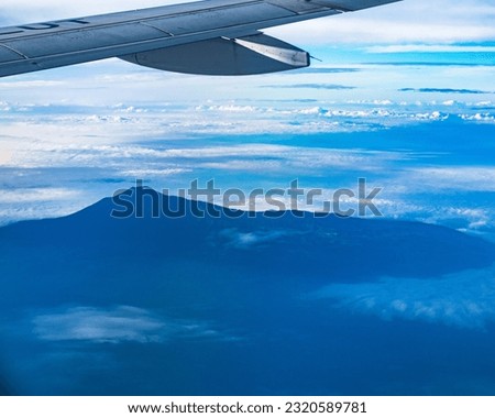 The majestic Mount Slamet, the highest peak in Central Java, Indonesia, captivates from above, with its grandeur showcased against a backdrop of clear blue skies and fluffy clouds.