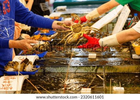 At a seafood vendor of a bustling fish market in Zhuwei, Taoyuan, Taiwan, a customer buying a live crab which is picked from the water tank with a smell of seafood filling in the air of a wet market