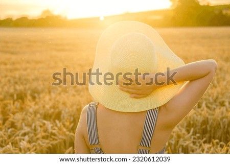 Against a backdrop of vivid sunflowers, a young lady elegantly stands, her straw hat adding a touch of charm
