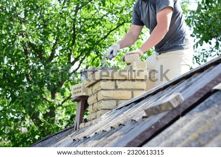 Bricklayer repair brick chimney on asbestos house rooftop Royalty-Free Stock Photo #2320613315