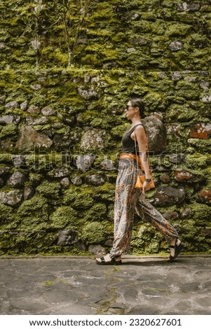 Walking young stylish girl on temple wall background. Puru Gunung Kawi ancient architecture, female tourist in rocky temple